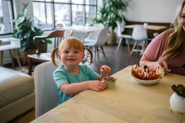 Young child with red hair eating ice cream in a bright ice cream shop.