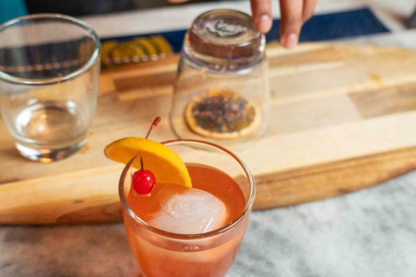 A bartender has a glass overtop of smoked dried fruit for a cocktail wiht an orange cocktail sitting on the table at Tequila House in Elizabethtown, Kentucky
