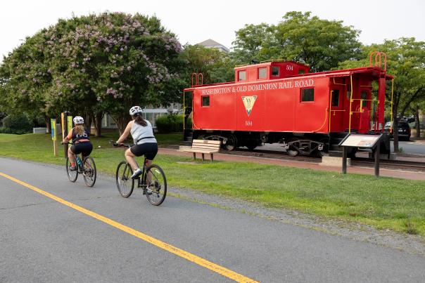Two People Cycling Next to a Lone Red Train Car on the Washington & Old Dominion Trail