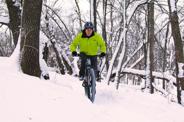 guy in green coat biking in the snow