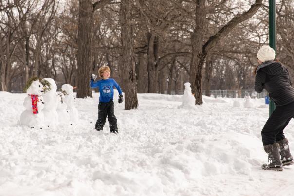 son and mom throwing snow balls while making snowmen