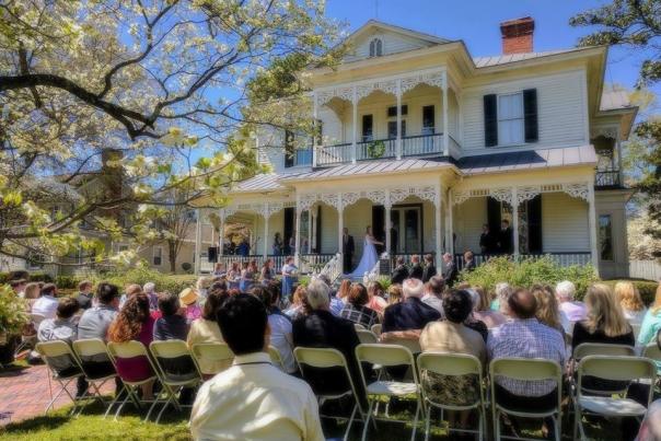 Outdoor wedding ceremony with guests seated on a lawn in front of the historic 1897 Poe House in Fayetteville, North Carolina.