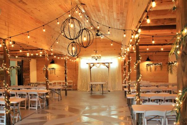 Rustic winter wedding reception space with wooden beams, greenery and string lights in a barn venue in Cumberland County, NC.