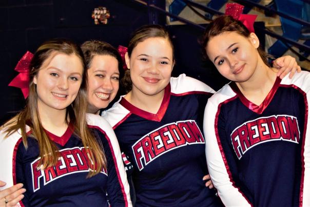 Cheerleaders standing together and smiling during a competitive cheer event, wearing matching uniforms.