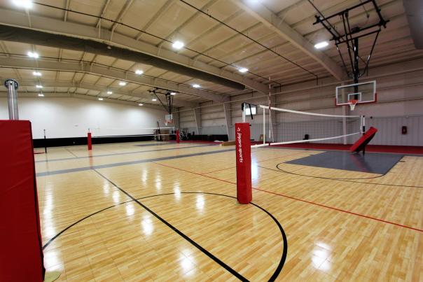 Indoor multi-court sports facility with volleyball nets and basketball hoops set up on hardwood flooring.