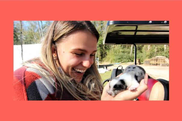 A woman laughs while gently cradling a newborn puppy that, at first glance, looks like a piglet.