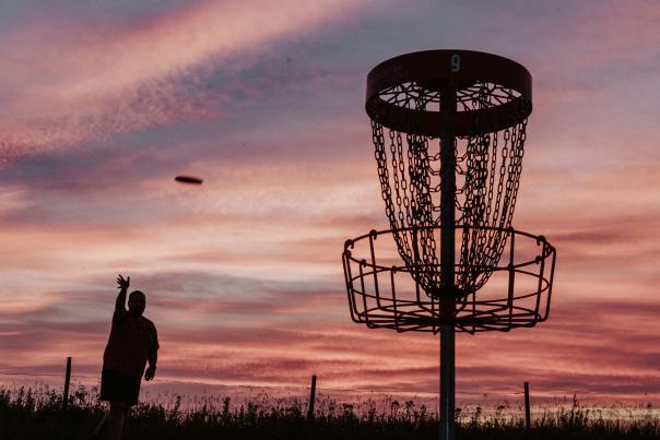 image of a dis golf player throwing their frisbee toward a goal basket at dusk