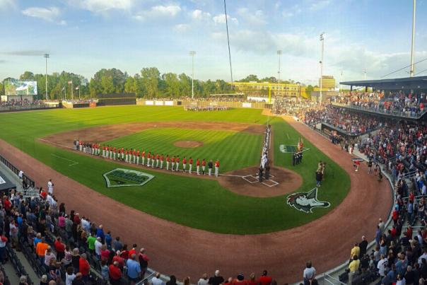 Fans filling Segra Stadium in Fayetteville, NC, for a baseball game as players line up on the field during the national anthem.