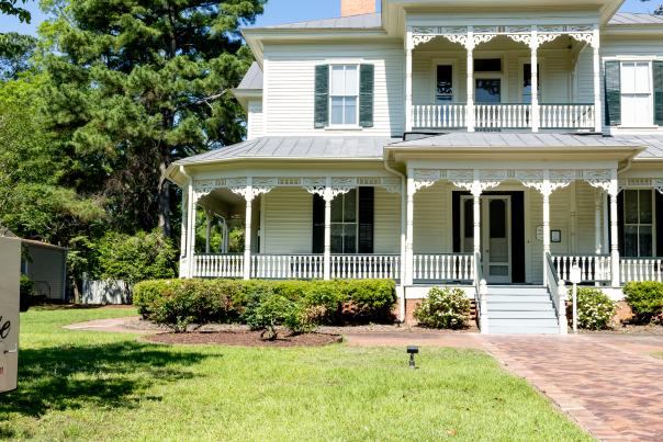 Front view of the historic 1897 Poe House in Fayetteville, North Carolina, surrounded by greenery and featuring its signature wraparound porch and ornate trim.