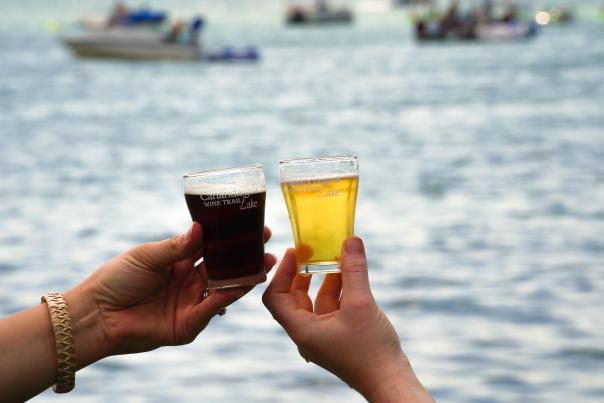 People holding Canandaigua Lake Wine Trail branded cups in front of Canandaigua lake at the Canandaigua Lakefront Art Show