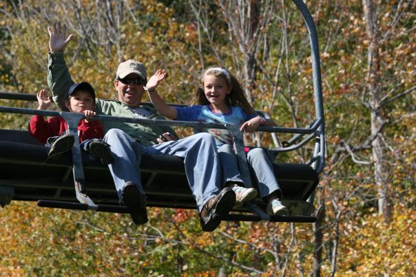 Family waving from a chair lift with fall trees in the background