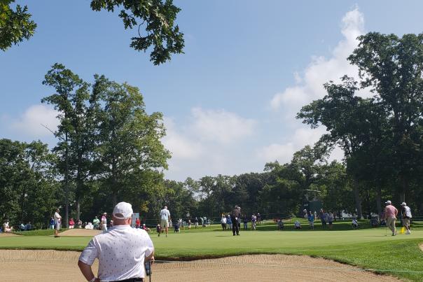 A man watches in the foreground as a golfer gets ready for a shot.
