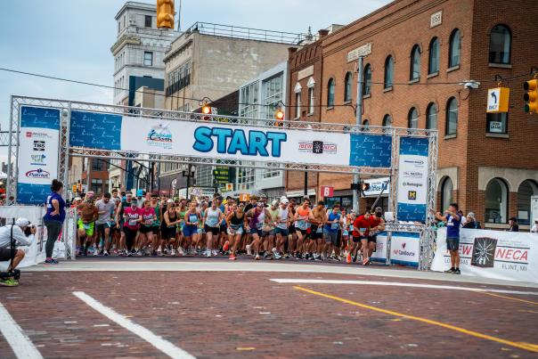 A large group of runners line up under the start banner for the 2025 Crim Festival of Races