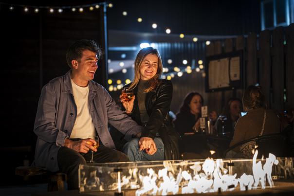 A man and woman sitting outside at Fenton Winery & Brewery, drinking wine by a fire.