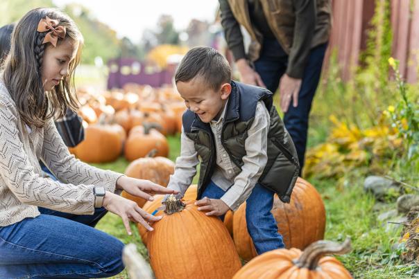 A mother and child look at a large pumpkin with excitement, as they sit in a pumpkin patch.