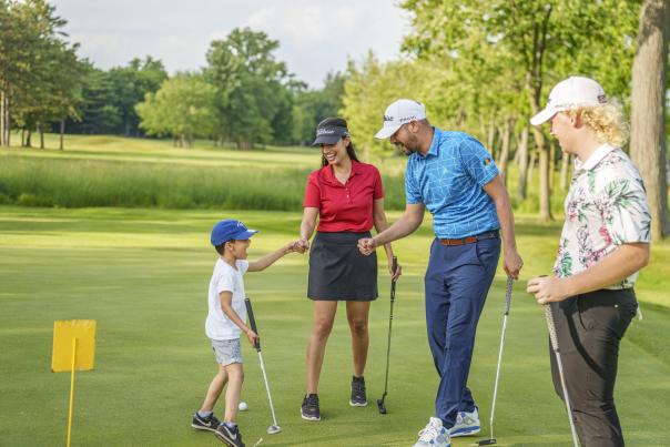 A young boy enjoys some golfing fun and celebrates with three adults on the course.