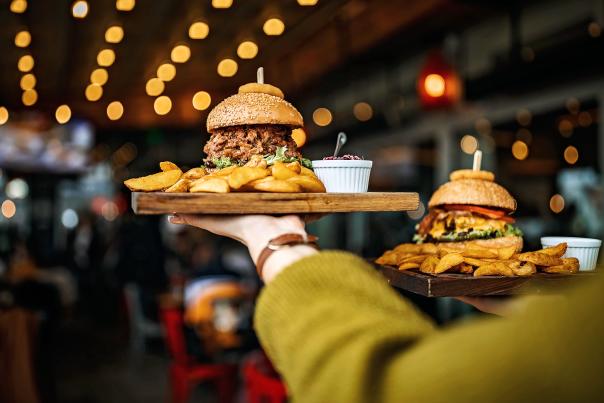 A server brings two BBQ sandwiches to a table in a busy restaurant.