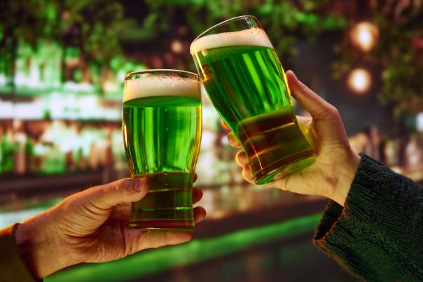 Two hands cheers-ing green beers in a bar.