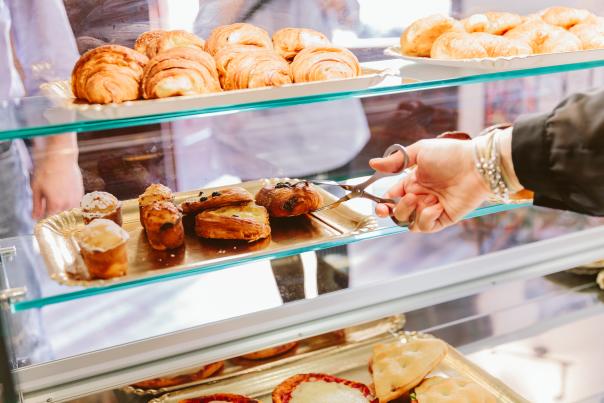 A hand with bracelets on moves to retrieve a pastry from a display counter to serve to a customer.