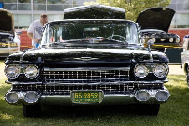 A black classic car is front and center on the grass at the Sloan Museum Auto Fair.