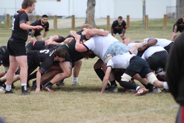 Two rugby teams preparing for play to resume as they are huddled together, heads bowed toward one another, and arms locked.