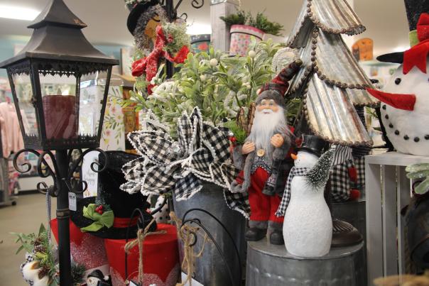 A mix of holiday items in a shop featuring a black lamp, small snowman, small Santa, snowman head, and an arrangement of pine tree branches in a vase.