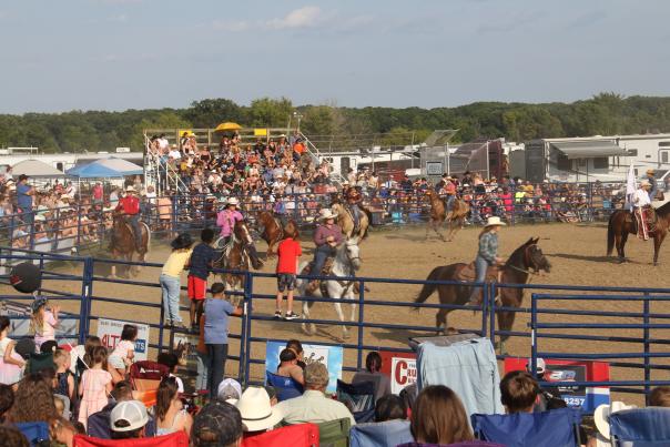 An image of a packed crowd watching as horses and their riders parade around a ring at the Gaines Rodeo.