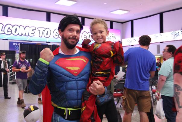 A man dressed as Superman holding a young child dressed as superhero the Flash.
