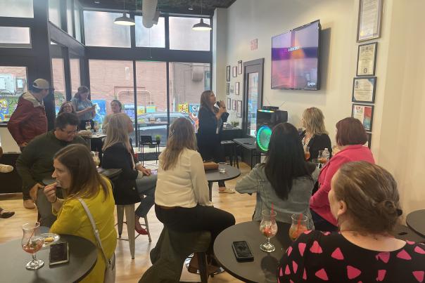 People sitting at tables watching a woman sing karaoke in a business.