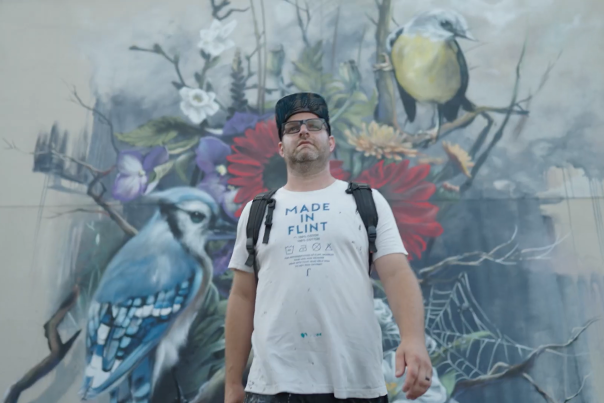 An artist standing before a mural he painted on the side of a building.