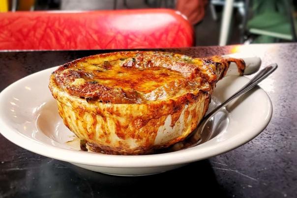 A bowl of French Onion Soup on a white dish with a spoon.