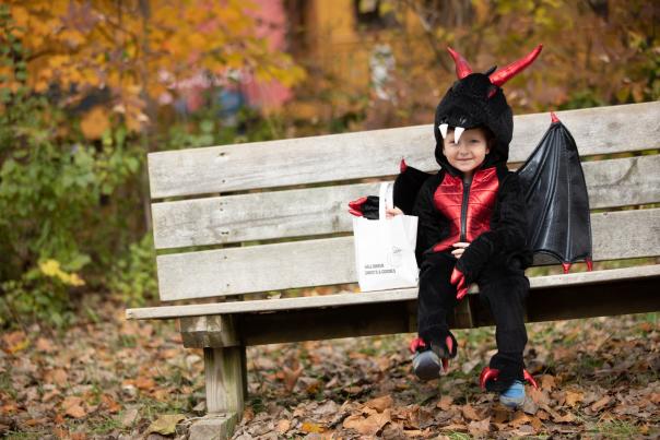 A child dressed as a dragon for Halloween sits on a bench.