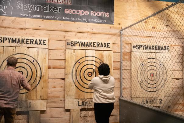 Two people stand at separate targets after having thrown axes at wooden targets at Spymaker Axe Throwing.