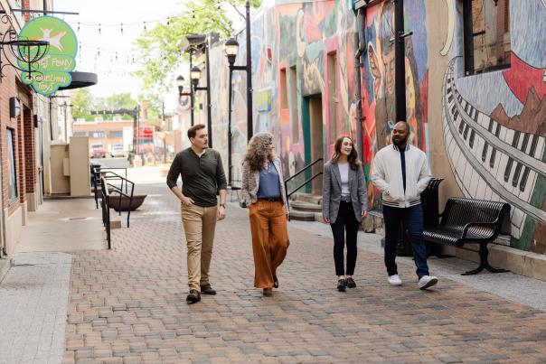 Four people walking in an alley with a colorful mural on the wall