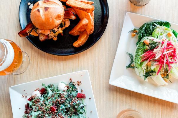 A photo of quinoa salad, a glass of wine, a glass of beer, a burger and fries, house-made chips and a salad, all plated seperately