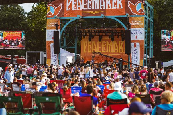 A crowd of people enjoy a band performing on a vibrant stage at Peacemaker Music Festival in Fort Smith.