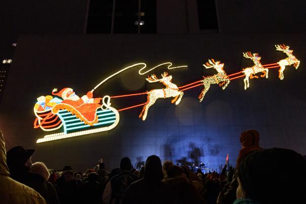 large holiday lights display on the side of a building showing santa in his sleigh being pulled by reindeer