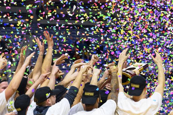 Basketball team celebrating with a trophy as confetti falls around them