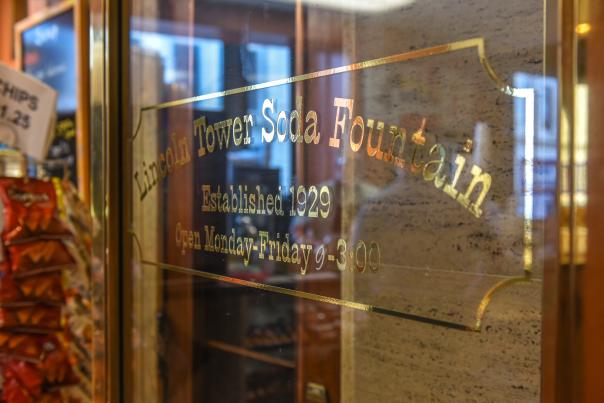 Gold letters writing "Lincoln Tower Soda Fountain" are on a glass door
