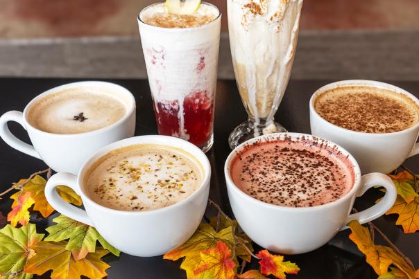 Six fall drinks on a table surrounded by leaves.