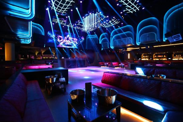 Dark nightclub with purple and blue lights shining all around the room.