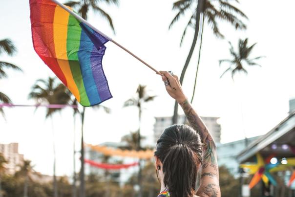 The back of a woman with tattoos waving a rainbow flag