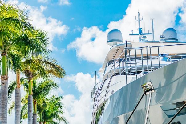 Looking up at a Super Yacht next to palm trees with a blue sky with puffy white clouds