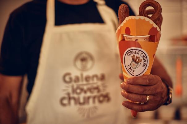 A person holding a container of churros, wearing a white apron that says, "Galena loves churros."