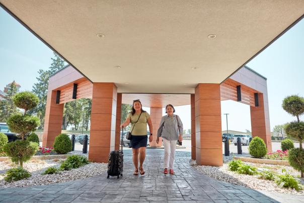 Two people walking into a hotel, pushing a suitcase.