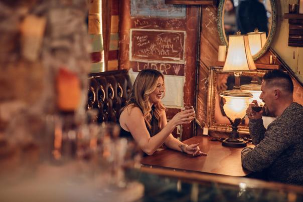 Two people sitting in an eclectic space, having drinks, sitting in a booth.