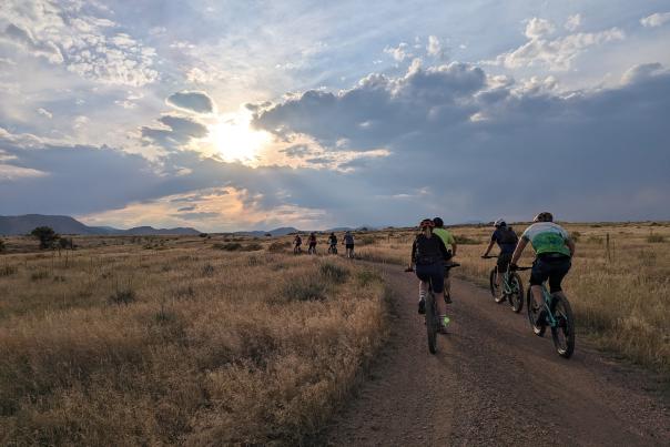 A group of bikers on top of a table mountain mesa in Golden CO as the sun nears the horizon moutains in the evening behind clouds.