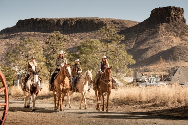 Four cowgirls riding horses in Golden Colorado with Castle Rock on South Table Mountain in the background