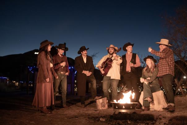 People around a campfire in Golden in western attire, one person is playing a guitar