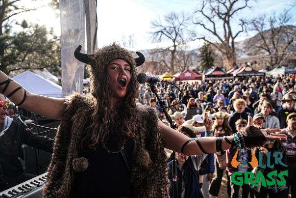 A woman dressed in Viking regalia on stage at UllrGrass Music and beer festival with a large crowd behind listening to the music in Parfet Park, downtown Golden, CO.